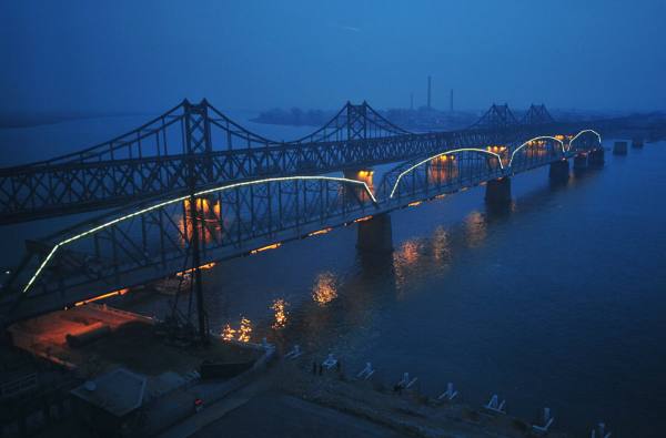 Dusk falls over the Yalu River, which separates the North Korean town of Siniuju (opposite) from the Chinese city of Dandong, as lights are turned on along the Yalu River bridge, also known as the no-name bridge. The full-length bridge built right beside the no-name bridge remains busy during the day time as trucks, trains and other vehicles transport goods back and forth (Frederic J. Brown/AFP/Getty Images